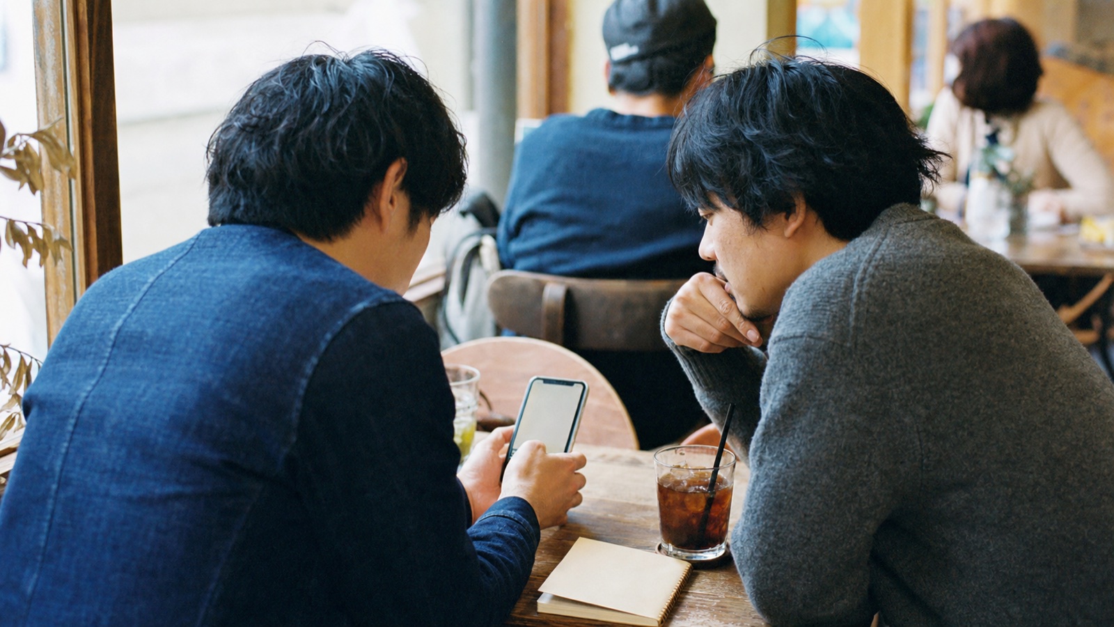 カフェでスマートフォンを見ながら地下アイドルについて話す二人のイメージ